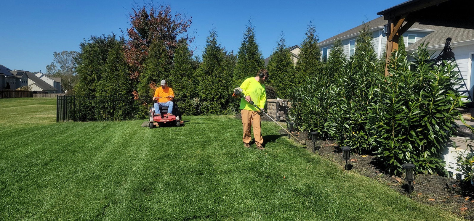 Landscaping crew mowing and trimming a residential hedge line